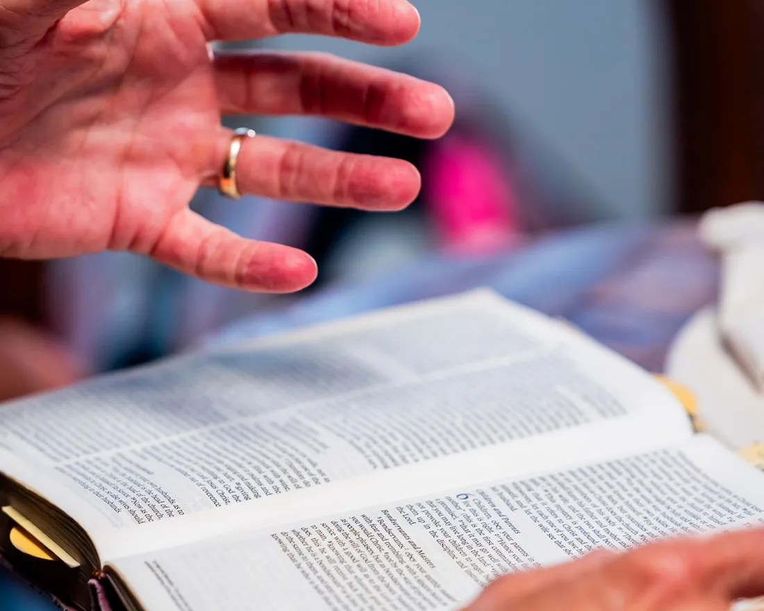 An open hand resting in prayer over an open Bible